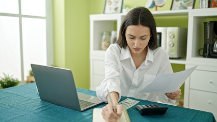 Young beautiful hispanic woman using laptop accounting at dinning room