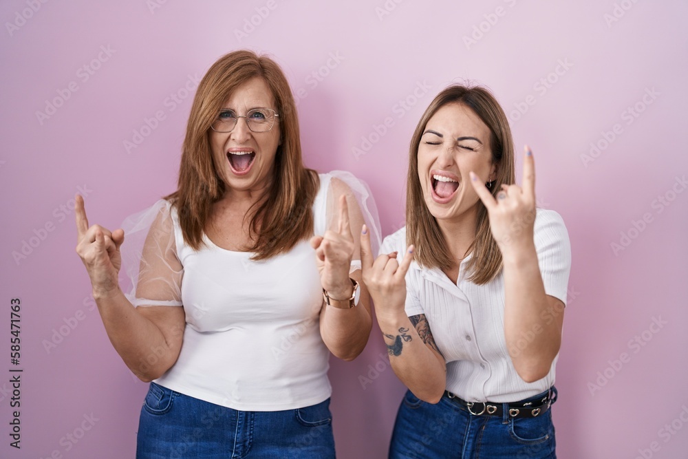 Poster hispanic mother and daughter wearing casual white t shirt over pink background shouting with crazy e