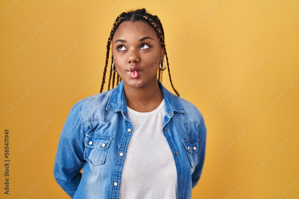 Poster African american woman with braids standing over yellow background making fish face with lips, crazy and comical gesture. funny expression.