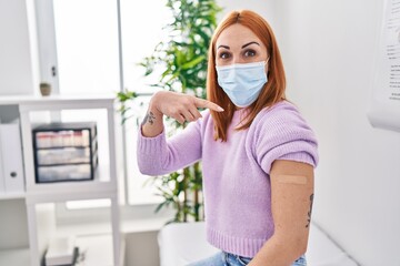 Young woman getting vaccine showing arm with band aid smiling happy pointing with hand and finger