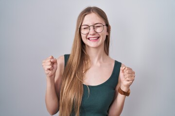 Young caucasian woman standing over white background excited for success with arms raised and eyes closed celebrating victory smiling. winner concept.