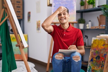 Young hispanic man drawing on art notebook stressed and frustrated with hand on head, surprised and...