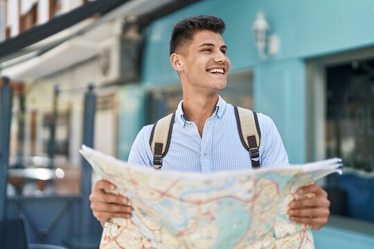 Young hispanic man student smiling confident holding city map at street