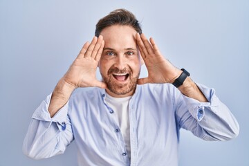Naklejka premium Middle age caucasian man standing over blue background smiling cheerful playing peek a boo with hands showing face. surprised and exited