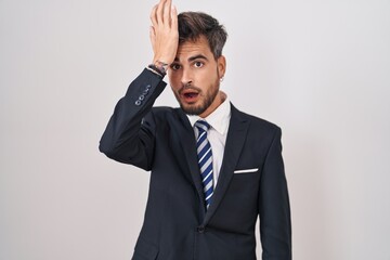 Young hispanic man with tattoos wearing business suit and tie surprised with hand on head for mistake, remember error. forgot, bad memory concept.