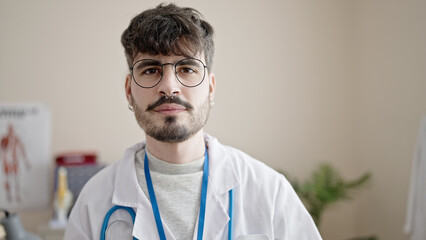 Young hispanic man doctor standing with serious expression at clinic