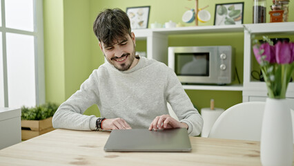 Young hispanic man opening laptop at dinning room