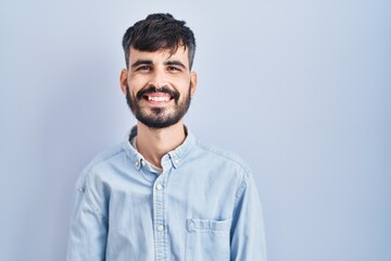 Young hispanic man with beard standing over blue background with a happy and cool smile on face. lucky person.