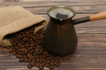 Burlap bag with black coffee beans. Turk with coffee. On a brown background.