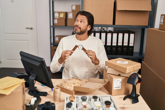 Handsome middle age man working at small business ecommerce repairing watches smiling looking to the side and staring away thinking.