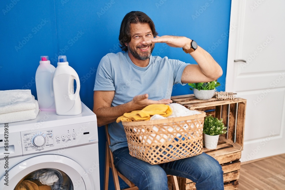 Wall mural Handsome middle age man waiting for laundry gesturing with hands showing big and large size sign, measure symbol. smiling looking at the camera. measuring concept.