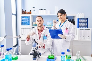 Two young people working at scientist laboratory pointing finger to one self smiling happy and proud