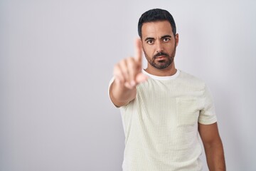 Hispanic man with beard standing over isolated background pointing with finger up and angry expression, showing no gesture