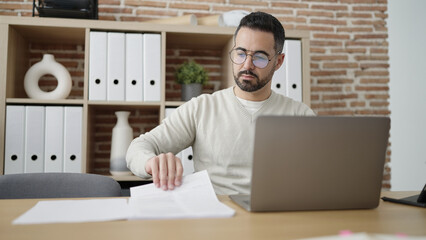 Young hispanic man business worker using laptop reading document at office