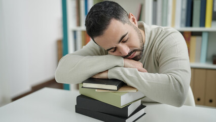 Young hispanic man student sleeping with head on books at library university