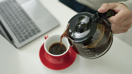 Young hispanic man pouring coffee on cup at home