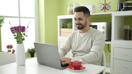 Young hispanic man using laptop sitting on table at home