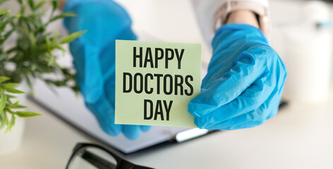 Paper with text HAPPY DOCTORS DAY in hands and stethoscope on white background - Powered by Adobe
