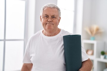 Middle age grey-haired man smiling confident holding yoga mat at home