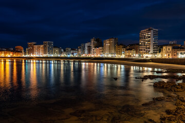 Fototapeta na wymiar Promenade at night with reflections of lights and buildings in the sea water, Gijon, Asturias.