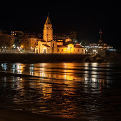 Fototapeta premium Old stone church located by the sea at night with reflections in the water, Gijon, Asturias.