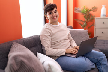 Non binary man using laptop sitting on sofa at home