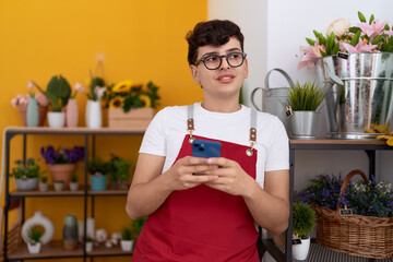 Non binary man florist smiling confident using smartphone at flower shop