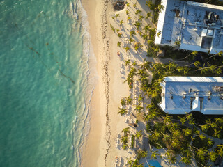 Aerial view of a tropical beach. On the sandy shore roofs of houses among palm trees. Clear emerald sea. Beautiful nature, a heavenly place to relax, exotic.