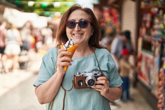Senior woman tourist holding camera eating ice cream at street