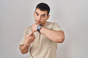 Young arab man wearing casual t shirt in hurry pointing to watch time, impatience, looking at the...