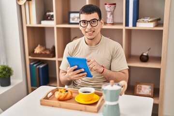 Young man having breakfast using touchpad at home