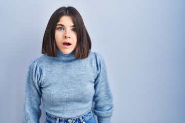 Young hispanic woman standing over blue background afraid and shocked with surprise and amazed expression, fear and excited face.