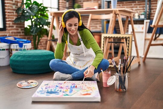 Young caucasian woman artist listening to music sitting on floor drawing at art studio