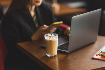 A girl works at a laptop in a cafe. Freelanser girl. Happy and successful girl works remotely.