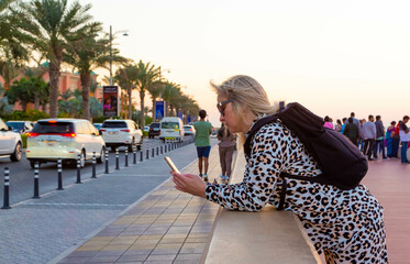 The photo shows a beautiful blonde tourist who enjoys the hospitality of Dubai. Her smile is bright and welcoming, and her hair is flying in the wind, giving her a certain playfulness.