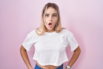 Young blonde woman standing over pink background afraid and shocked with surprise and amazed expression, fear and excited face.