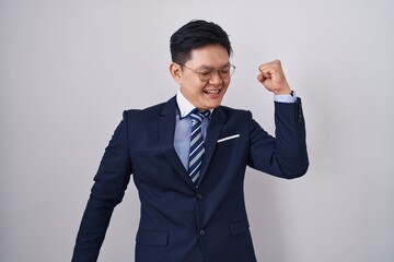 Young asian man wearing business suit and tie dancing happy and cheerful, smiling moving casual and confident listening to music