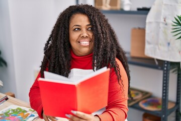 Naklejka premium African american woman artist smiling confident reading book at art studio