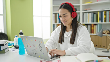Young beautiful hispanic woman student using laptop and headphones studying at university classroom