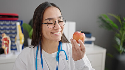 Young beautiful hispanic woman doctor smiling confident holding apple at clinic