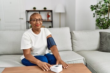 Senior african american woman smiling confident using tensiometer at home