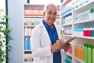 Middle age grey-haired man pharmacist writing on document at pharmacy