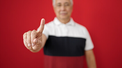 Middle age man with grey hair saying no with finger over isolated red background
