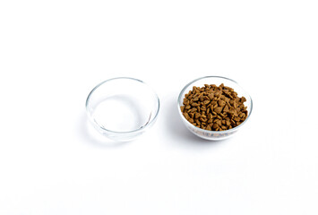 Dry pet food in a glass jar and bowl close-up on a white background. View from above