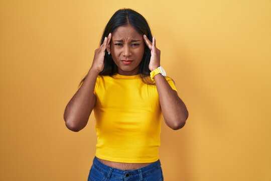 Young indian woman standing over yellow background with hand on head, headache because stress. suffering migraine.