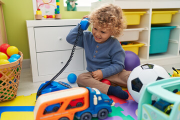 Adorable blond toddler playing with telephone toy sitting on floor at kindergarten