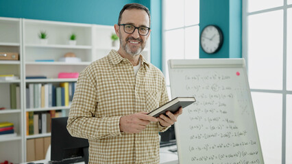 Middle age man teacher teaching lesson holding book at classroom
