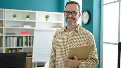 Middle age man teacher smiling confident holding clipboard at classroom