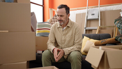 Middle age man sitting on sofa with serious expression at new home