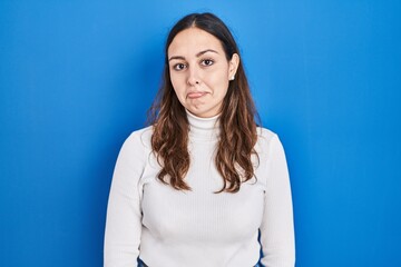 Young hispanic woman standing over blue background depressed and worry for distress, crying angry...